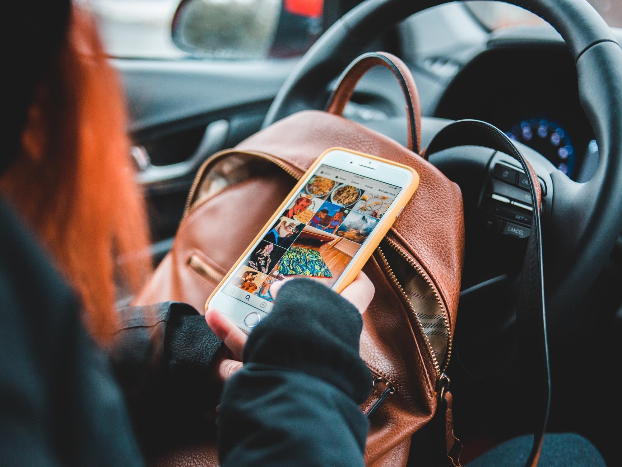 jovem com telemóvel na mão a ver instagram dentro de um carro